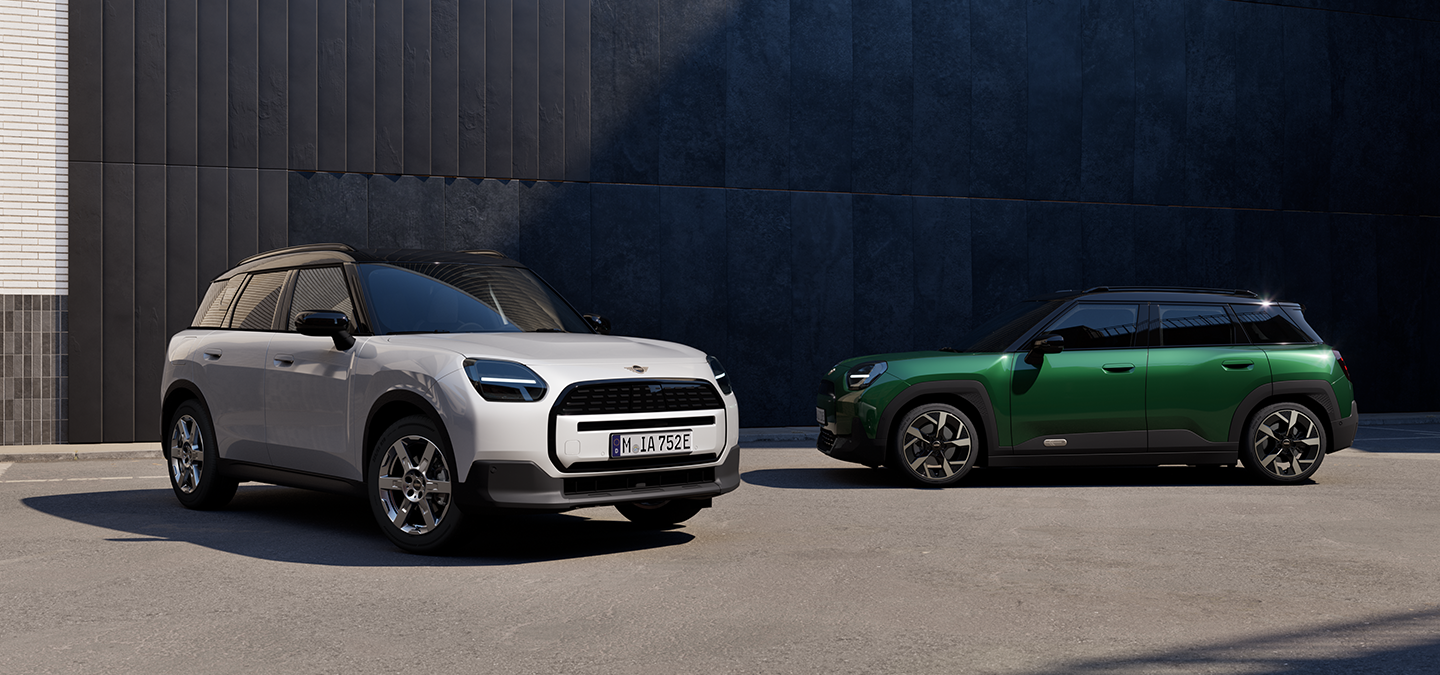 Vue avant et latérale du MINI Aceman Electric Nanuq White et British Racing Green avec toit noir en ville.