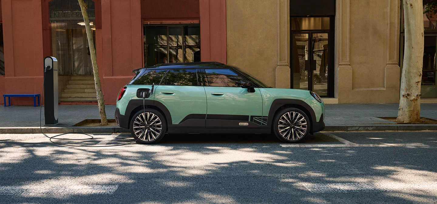 Vue latérale du MINI Aceman Electric Ocean Wave Green avec toit noir en charge en ville.