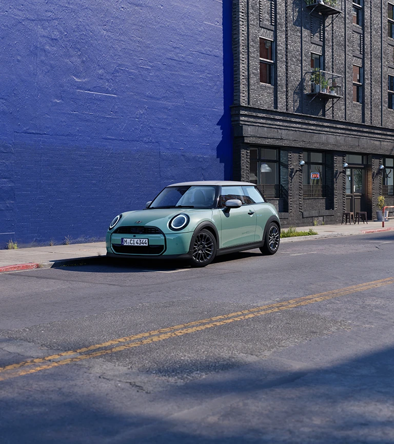 MINI Cooper stationné dans une rue urbaine à côté d’un mur bleu.