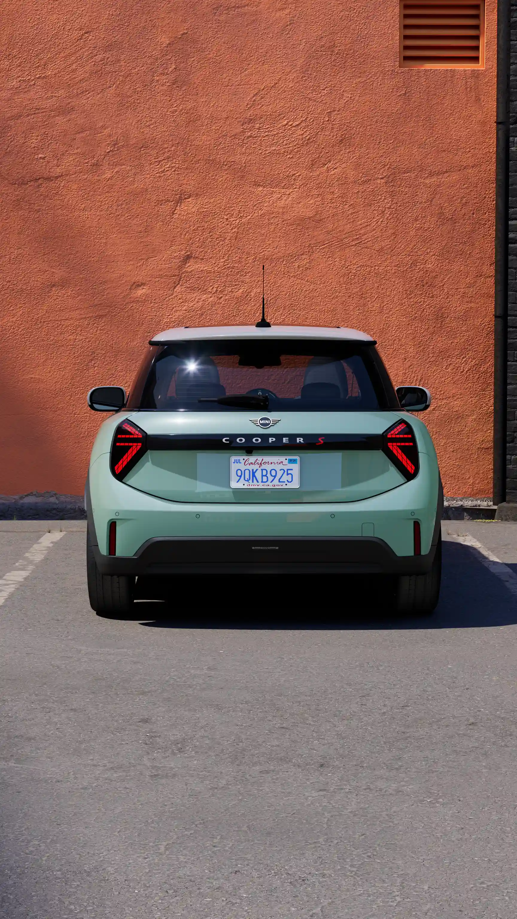 Vue arrière d’un MINI Cooper sur une place de parking marquée contre un mur orange.