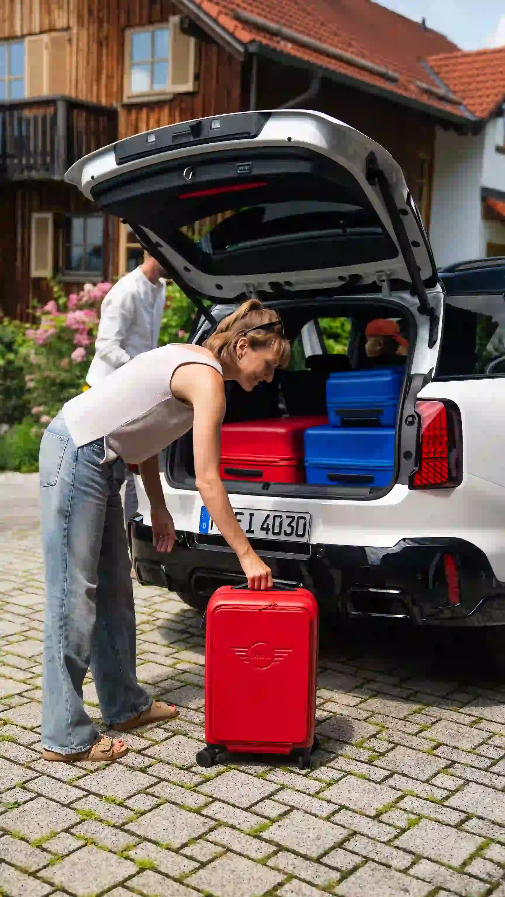 Personne chargeant une valise rouge dans le coffre d’un MINI Countryman avec des bagages bleus et rouges.