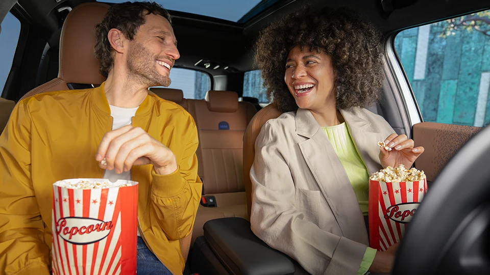 Deux personnes assises à l’intérieur d’un véhicule en train de déguster du pop‑corn.